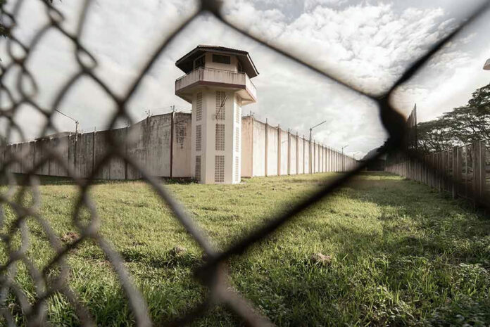 1587239341 View of prison watchtower through chain-link fence.