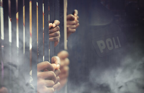 Hands gripping prison bars with a blurred police badge in the background