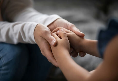 An adult hand holding a childs hand in a warm gesture