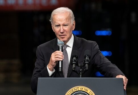 A man in a suit speaking into a microphone at a podium with a presidential seal