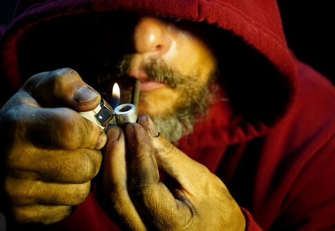 Person igniting a pipe, wearing a red hoodie.